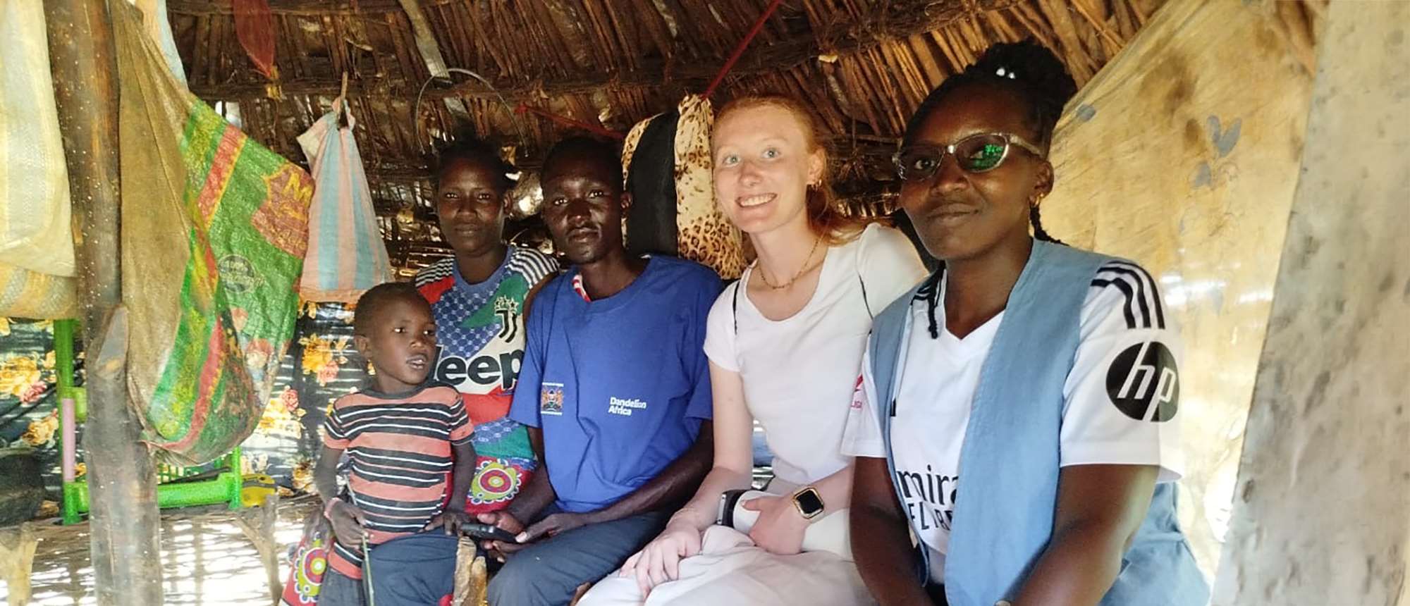 Four adults and a child sitting in a grass hut